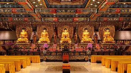 A temple hall with five golden Buddha statues under an ornate ceiling